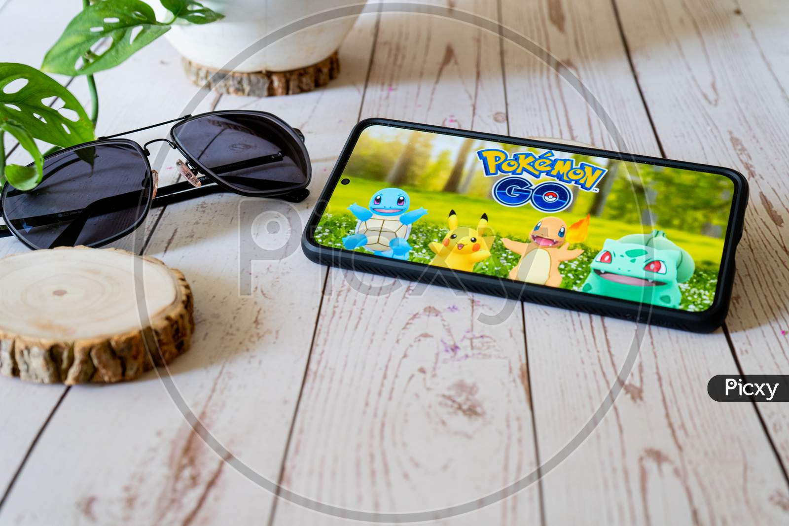 Famous Augmented Reality Virtual Game Pokemon Go Playing On A Mobile Phone On A Wooden Table Outdoors With Plants Goggles Showing People Enjoying This Multiplayer Game