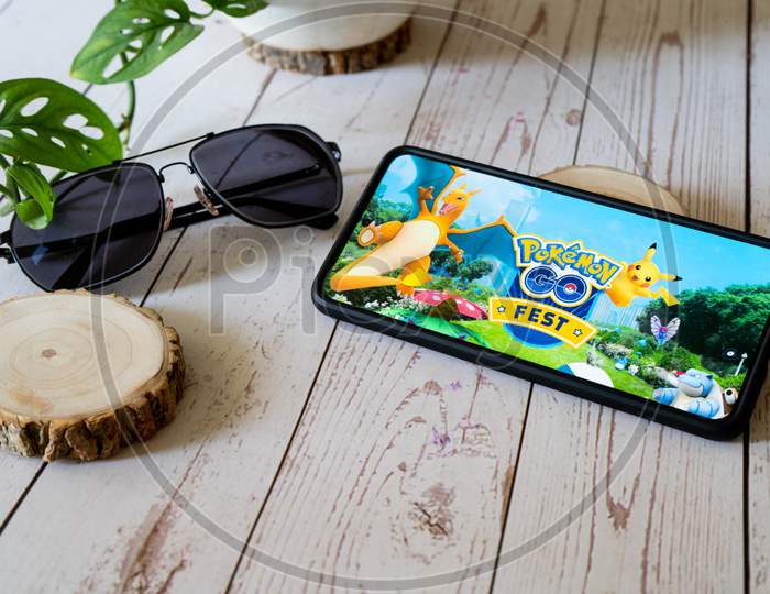 Famous Augmented Reality Virtual Game Pokemon Go Fest Playing On A Mobile Phone On A Wooden Table Outdoors With Plants Goggles Showing People Enjoying This Multiplayer Game