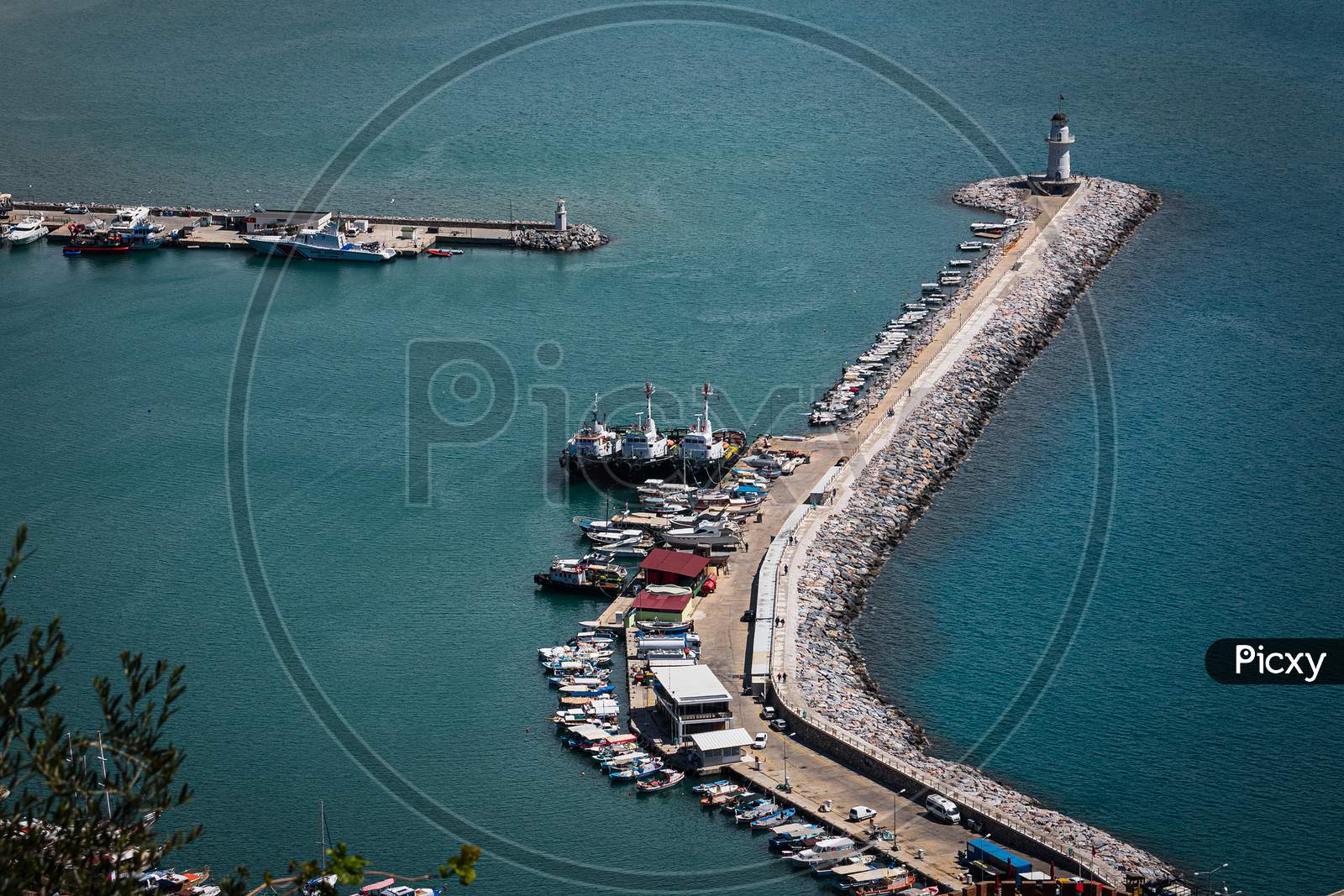 Top View Of A Pier  With A Beautiful White Lighthouse And A Pier With Many Boats And Yachts On The Background Of The Blue Sea