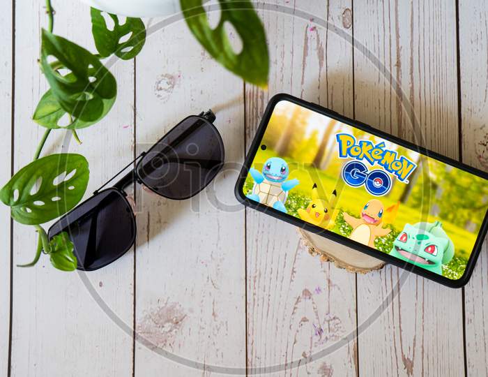 Famous Augmented Reality Virtual Game Pokemon Go Playing On A Mobile Phone On A Wooden Table Outdoors With Plants Goggles Showing People Enjoying This Multiplayer Game