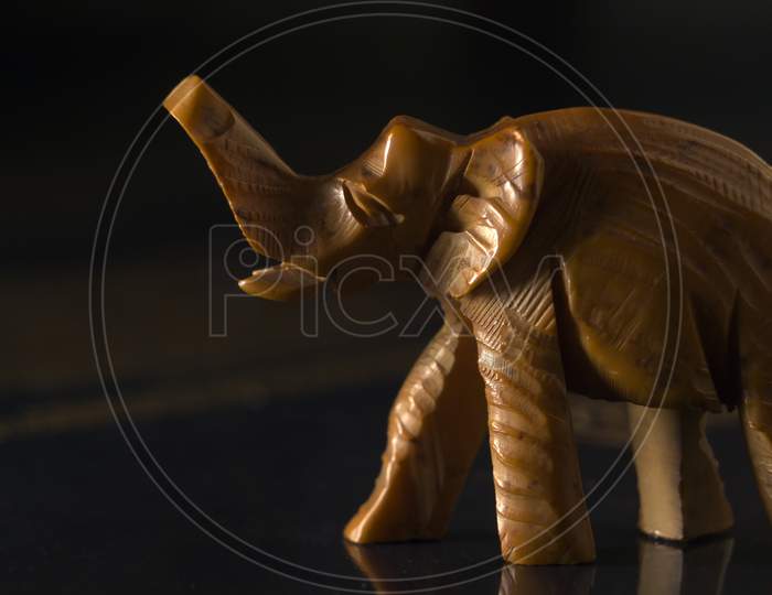 A Macro Close Up Shot Of A Carved Wooden Figure Of An Elephant With A Trunk Raised To The Top. Toy Elephant On Dark Background. Extreme Selective Focus With Copy Paste Text Space