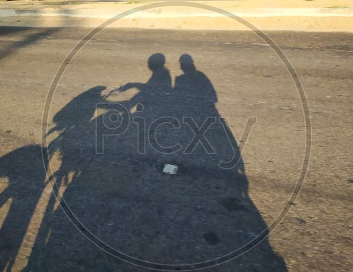 Closeup of shadow in a asphalt road men driving the bike and girl sitting back
