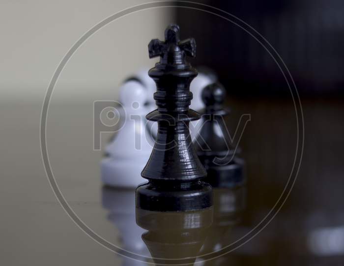 Extreme Close Up Macro Shot Of A Black Chess King Standing In Front Of Black And White Pawns Showing Leadership Concept. Selective Focus.