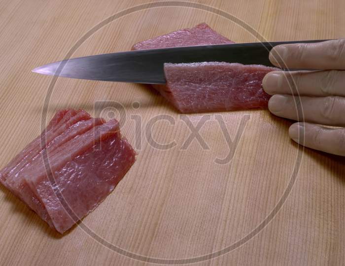 Closeup shot. Slicing fish meat with knife on a wooden table.