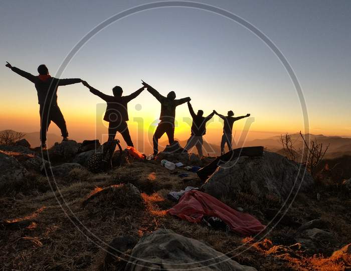 Four group of people standing together to create best shot of their journey in mountains  and guess what ? The perfect timing "Sun Set"