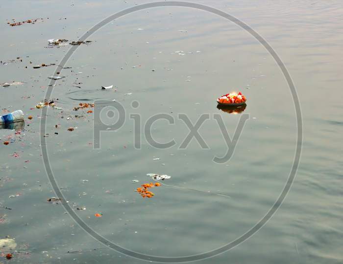 Diya Floating On A River Amongst Empty Plastic Bottle. Water Pollution.