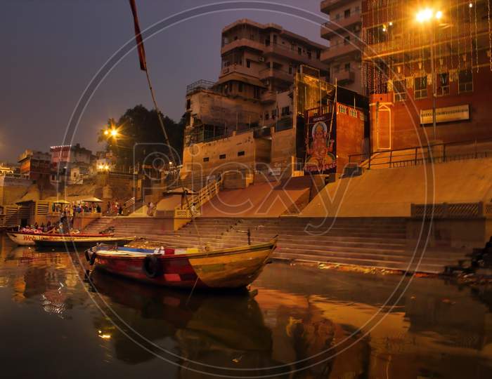 Varanasi, India - November 01, 2016: Bunch Of Wooden Boat Docked In Ganges River Next To Empty Ghat And Ancient Building Before Sunrise In State Of Uttar Pradesh. Hindu Holy Place With Ganesh Image