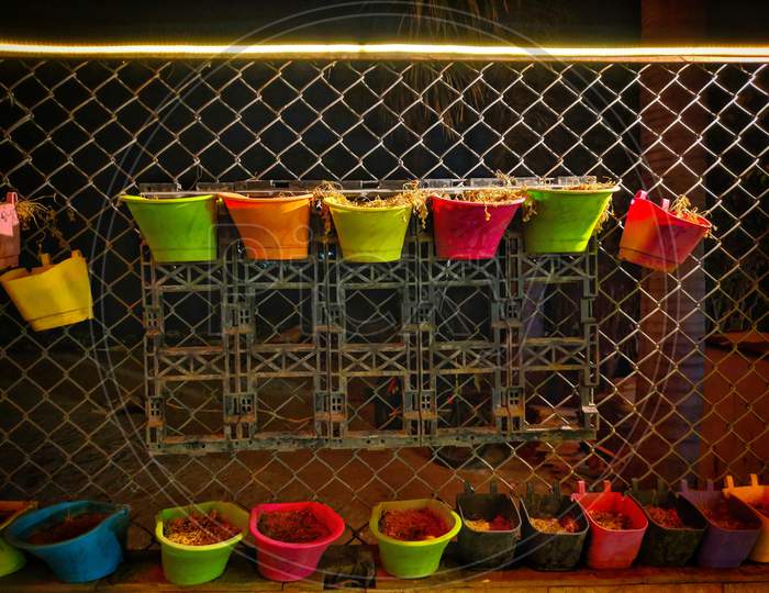 Arrangement Of Colorful Hanging Wicker Flowerpots With Green House Plants Against Decorative Black Grid,India.