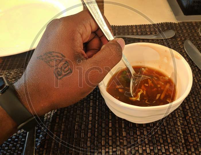 Hyderabad, India - May 06, 2021: Male Hands Holding A Bowl Of Hot Chicken Soup Served With Squash Seeds On White Tablecloth Background, From Above. Flat Lay. Homemade Autumn Food. Popular Thanksgiving Dish.