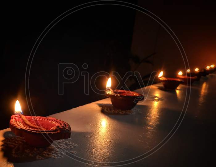 Happy Diwali Design With Diya Oil Lamps Elements On Dark Rangoli Background, Bokeh Sparkling Effect, Lit Diya Lamp On Street At Night, India.