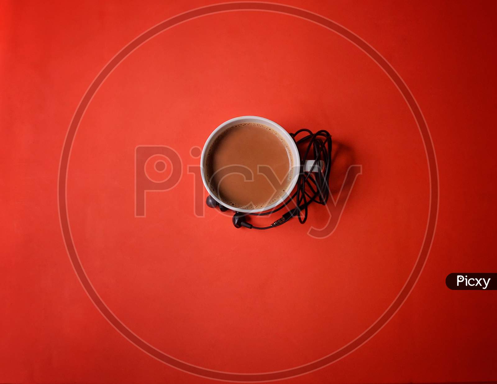 A White Cup Of Hot Espresso Coffee With Earphones On Orange Color Table Background. Top View With Copy Space.