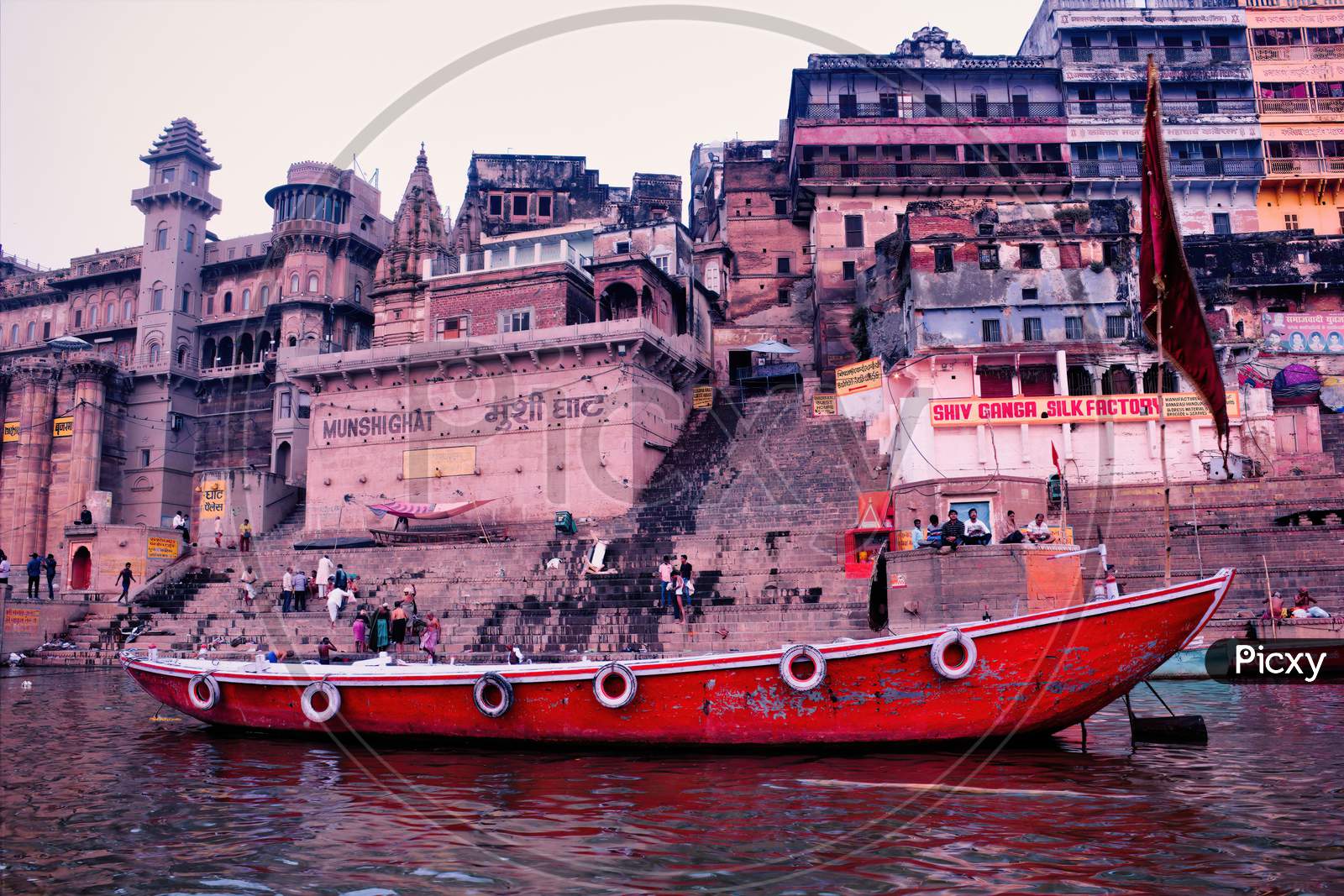 Varanasi, India - March 16, 2019: A Wooden Boats At River Ganga Docked Against Old Architecture Of Mushi Ghat In The Holy City Located In The State Of Uttar Pradesh.