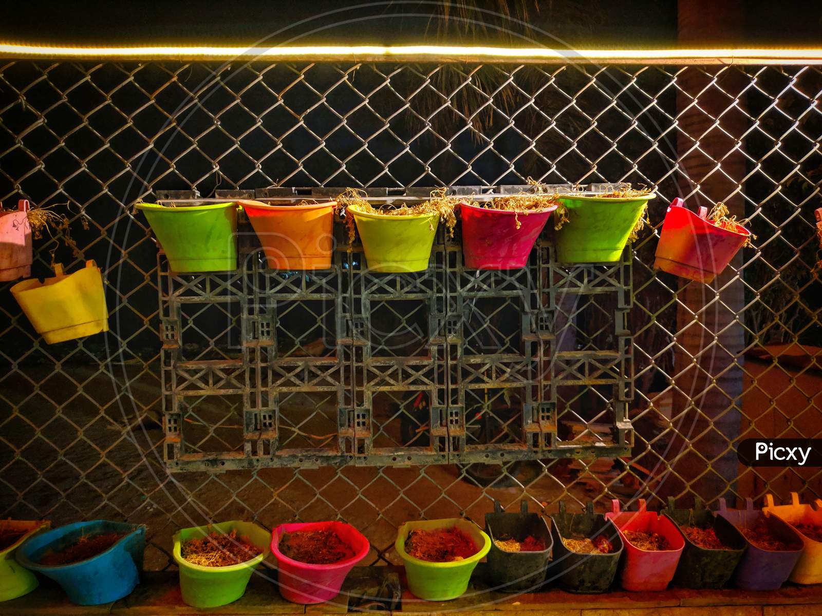 Arrangement Of Colorful Hanging Wicker Flowerpots With Green House Plants Against Decorative Black Grid,India.