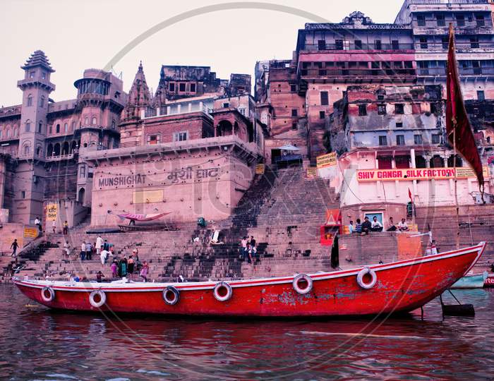 Varanasi, India - March 16, 2019: A Wooden Boats At River Ganga Docked Against Old Architecture Of Mushi Ghat In The Holy City Located In The State Of Uttar Pradesh.
