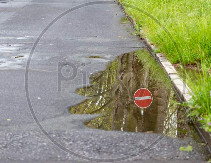 German road sign for one way and forbidden direction as restriction and prohibition for cars and road traffic as nice reflection on the water surface of a puddle after heavy rain on empty road