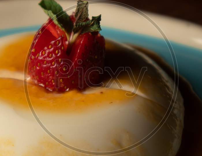 Caramel custard with a strawberry on top in a white and blue plate