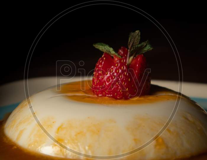Caramel custard with a strawberry on top in a white and blue plate