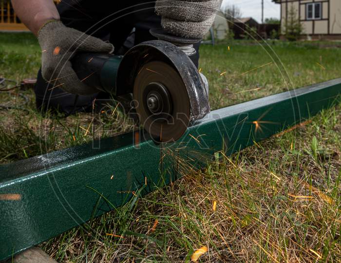 A Close-Up Of A  Welder Using A Metal Grinder To Cut A Metal On The Grass In The Village , Bright Flashes Flying In Different Directions