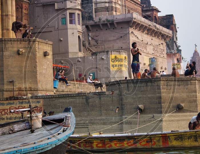 Varanasi, India - November 01, 2016: People Doing Random Activities At A Ganges River Bank Such As Yoga, Foreigner Taking Picture And Meditation In The Munshi Ghat. Holy Hindu Place In Uttar Pradesh