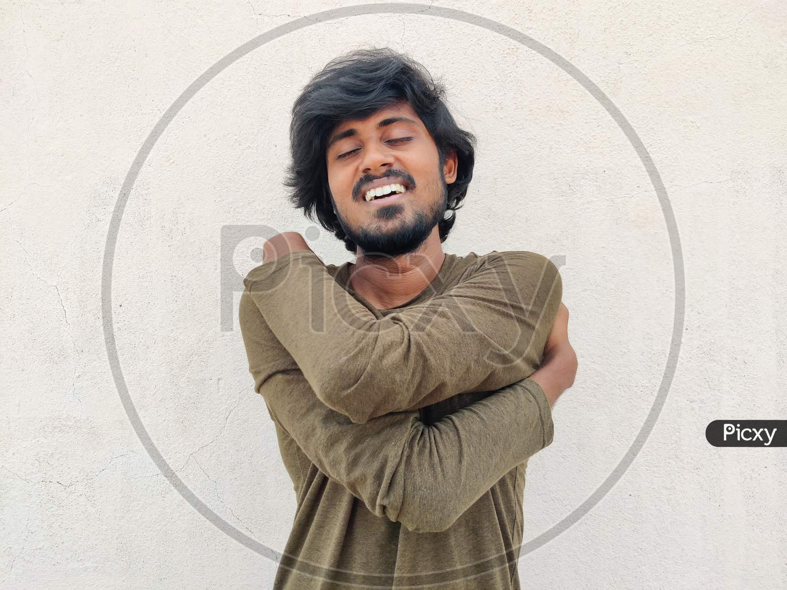 Young Smiling South Indian Tamil Man With Long Hairs, Beard Wearing Full Sleeves Is Hugging Himself Or Oneself. Self Care. White Background