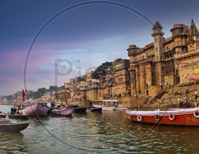 Varanasi, India - November 01, 2016: People And Tourists On Wooden Boat Sightseeing In Ganges River Near Munshi Ghat Against Ancient City Architecture As Viewed From A Boat During Morning Time