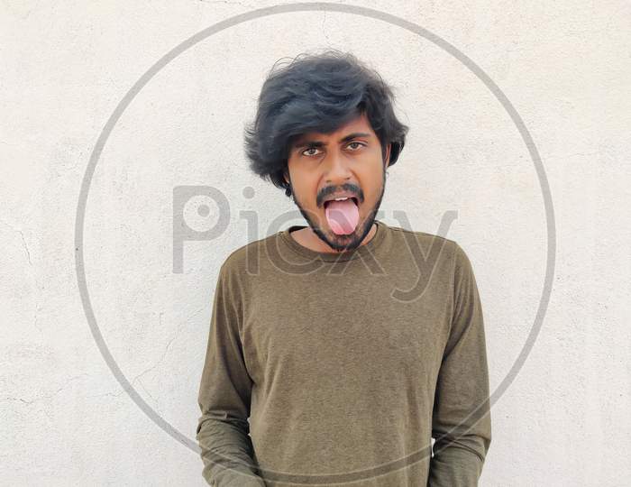 South Indian Handsome Man With Long Hairs Wearing Full Sleeves Showing His Tongue. White Background