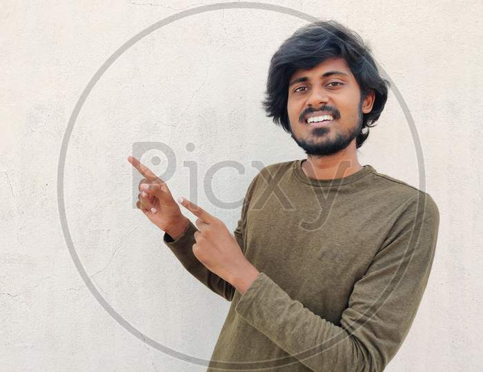 Super Cool Smiling Young Man With Beard And Long Hairs Wearing Formal Full Sleeves Pointing His Two Hands To Left Side. Copy Space. White Background