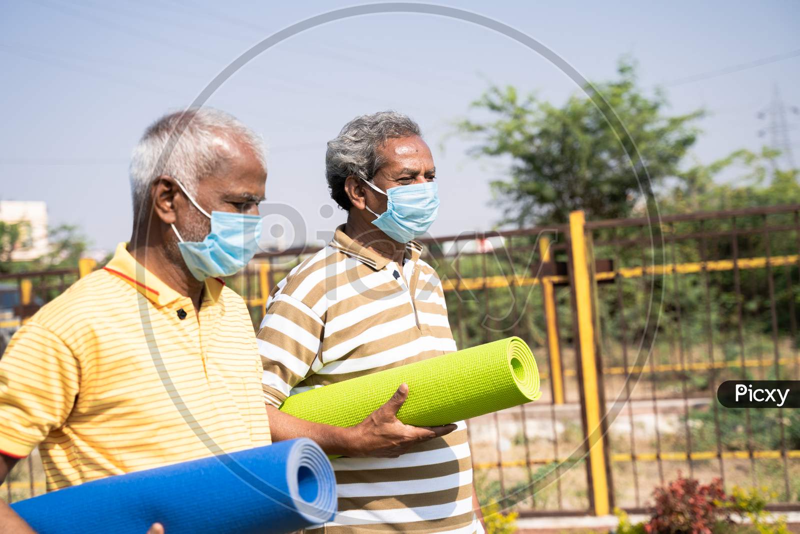 Two Senior Men With Medical Face Mask Holding Yoga Mat Coming To Park For Exercising During Morning - Concept Of New Normal Healthcare And Fitness During Coronavirus Covid-19 Pandemic.
