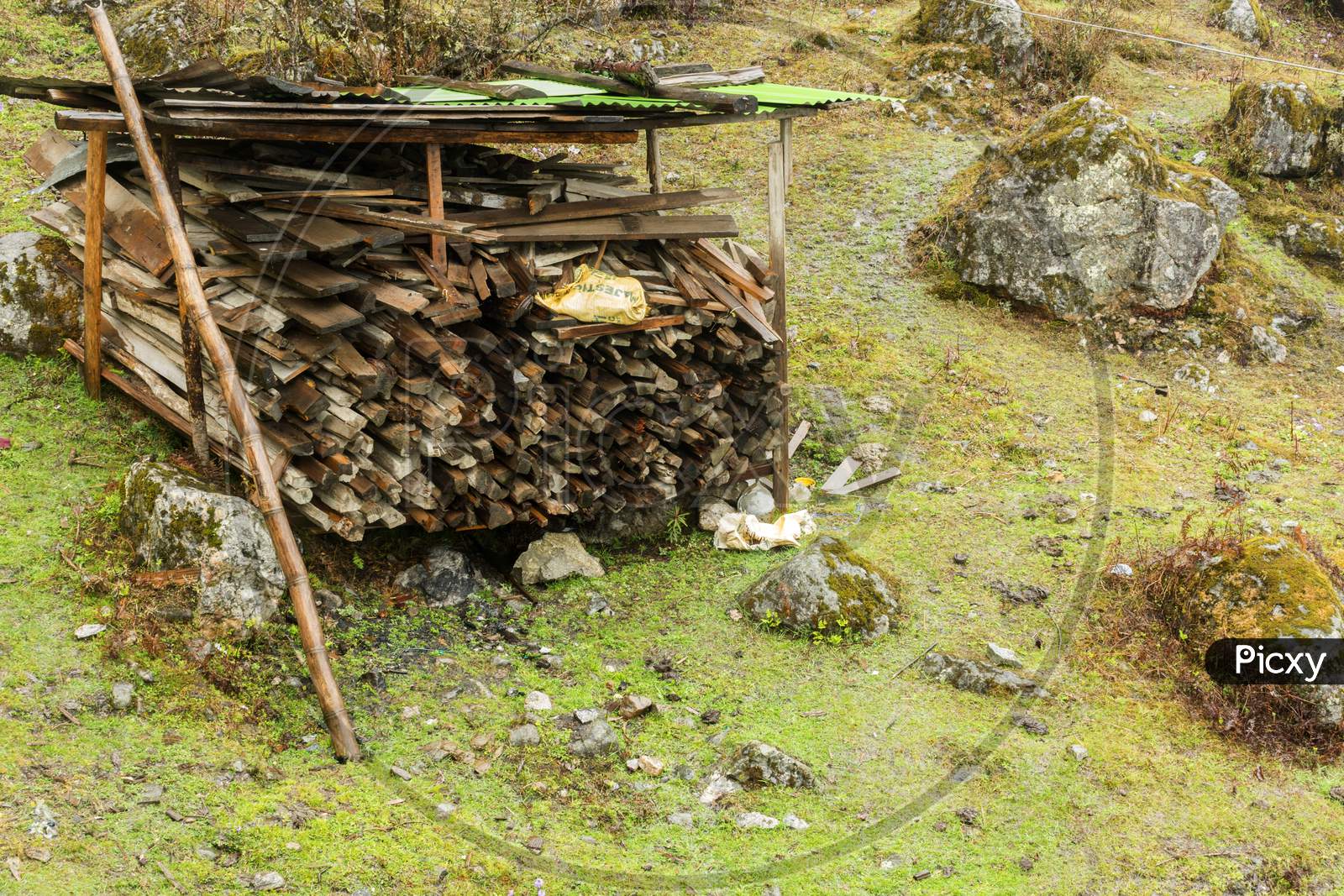 An Wooden Shade To Store Woods With Green Meadow In Background At Lachung Village Of North Sikkim.