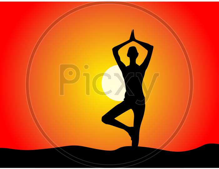 A silhouette of a woman standing in tree yoga position, meditating against sunset sky.