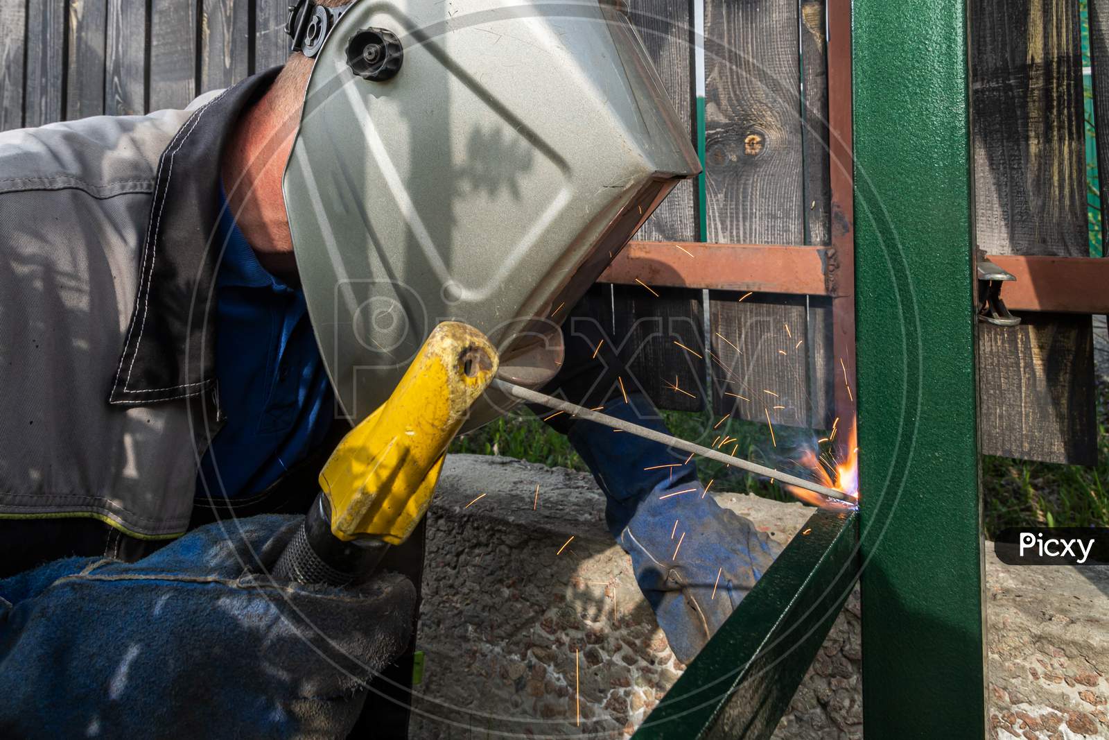 Close Up Of The A Welder Welds A Fence On The Construction Site In The Village. Construction On A Metal Frame.