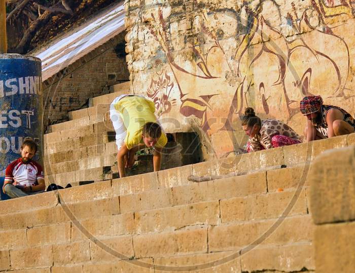 Varanasi, India - November 01, 2016: Bunch Of Foreigner Men In Hipster Style Doing Yoga In The Morning With A Trainer Against Wall With Graffiti In The City Of Banaras Situated In Uttar Pradesh
