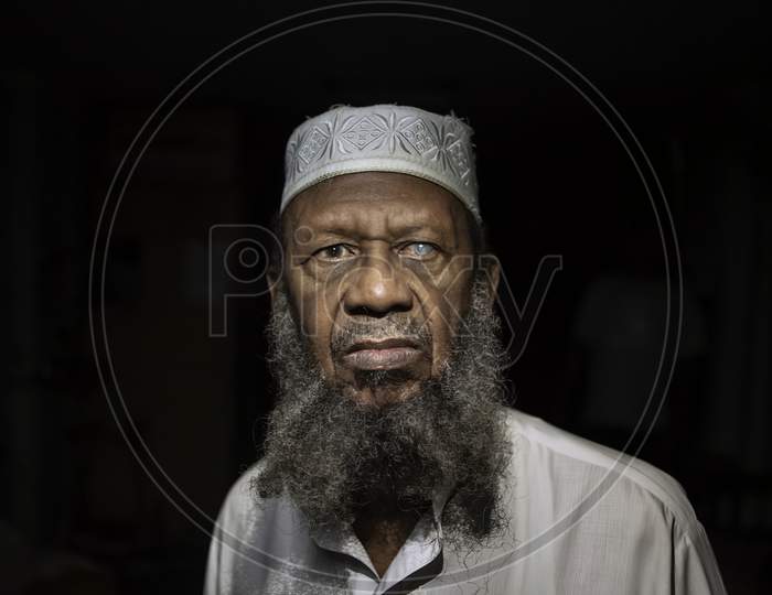 Close-up image of old aged muslim man wearing skull cap and kurta beard in face . Black background.
