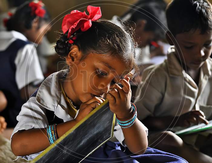Unidentified  girl  in government school uniforms sitting on floor, concentrate serious studying with books outdoors.