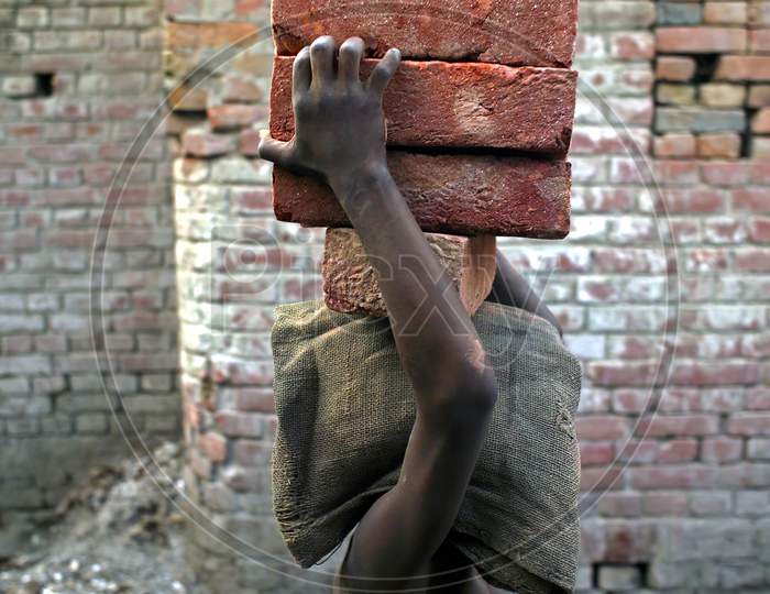A poor worker carrying heavy bricks on her head.