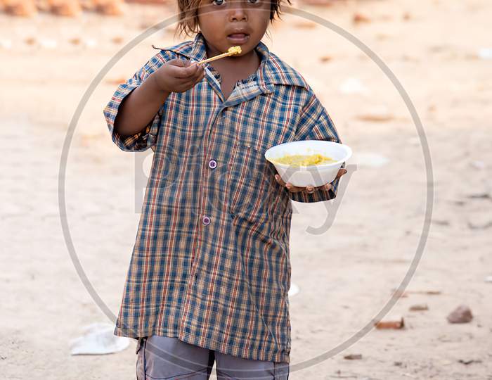 Unidentified poor kid eating food in the street. Poverty in india.