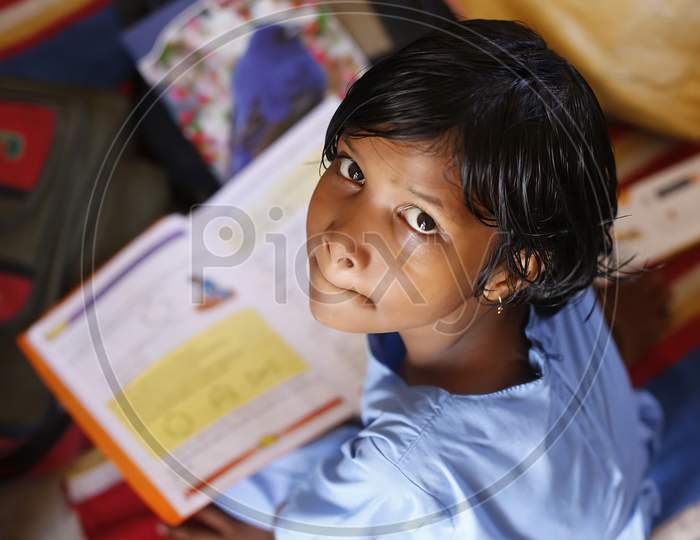 Unidentified  girl  in government school uniforms sitting on floor, concentrate serious studying with books outdoors.