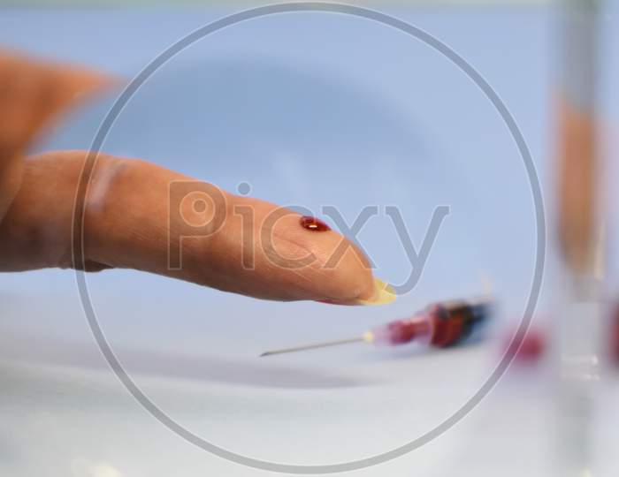 Finger blood test in focus with drop of blood
