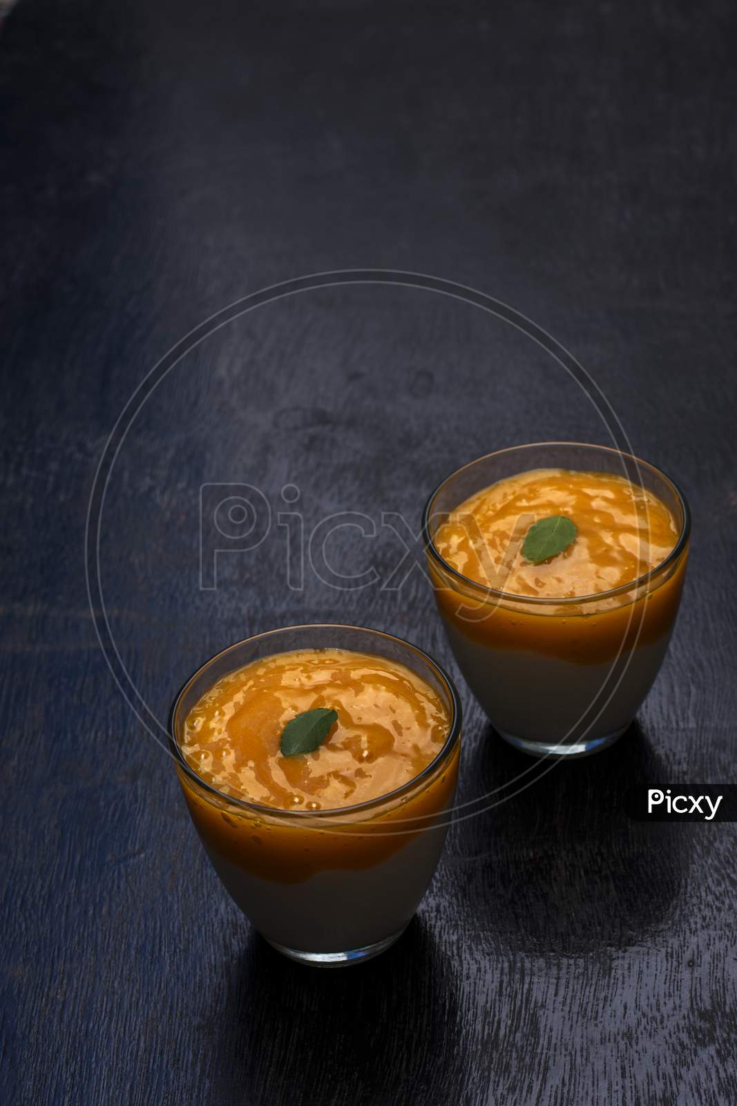 Two Glasses Of Delicious Mango Lassi Drink Decorated With Mint Leaves In Black Wooden Background.