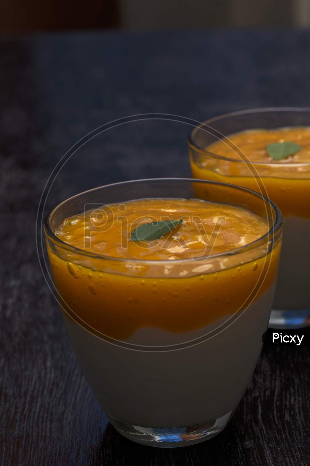 Two Glasses Of Delicious Mango Lassi Drink Decorated With Mint Leaves In Black Wooden Background.
