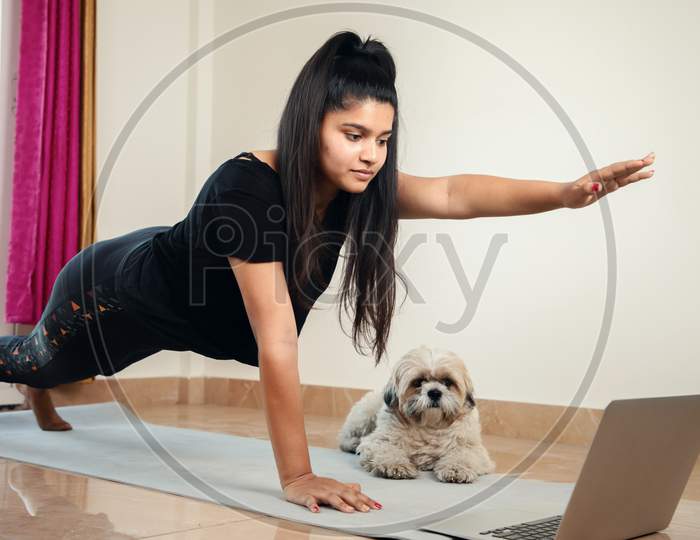 Young Millennial Girl Learning Yoga From Home During Online Class By Looking Laptop - Concept Of E-Learning, New Normal, Home Workout Due To Coronavirus Covid-19 Lockdown
