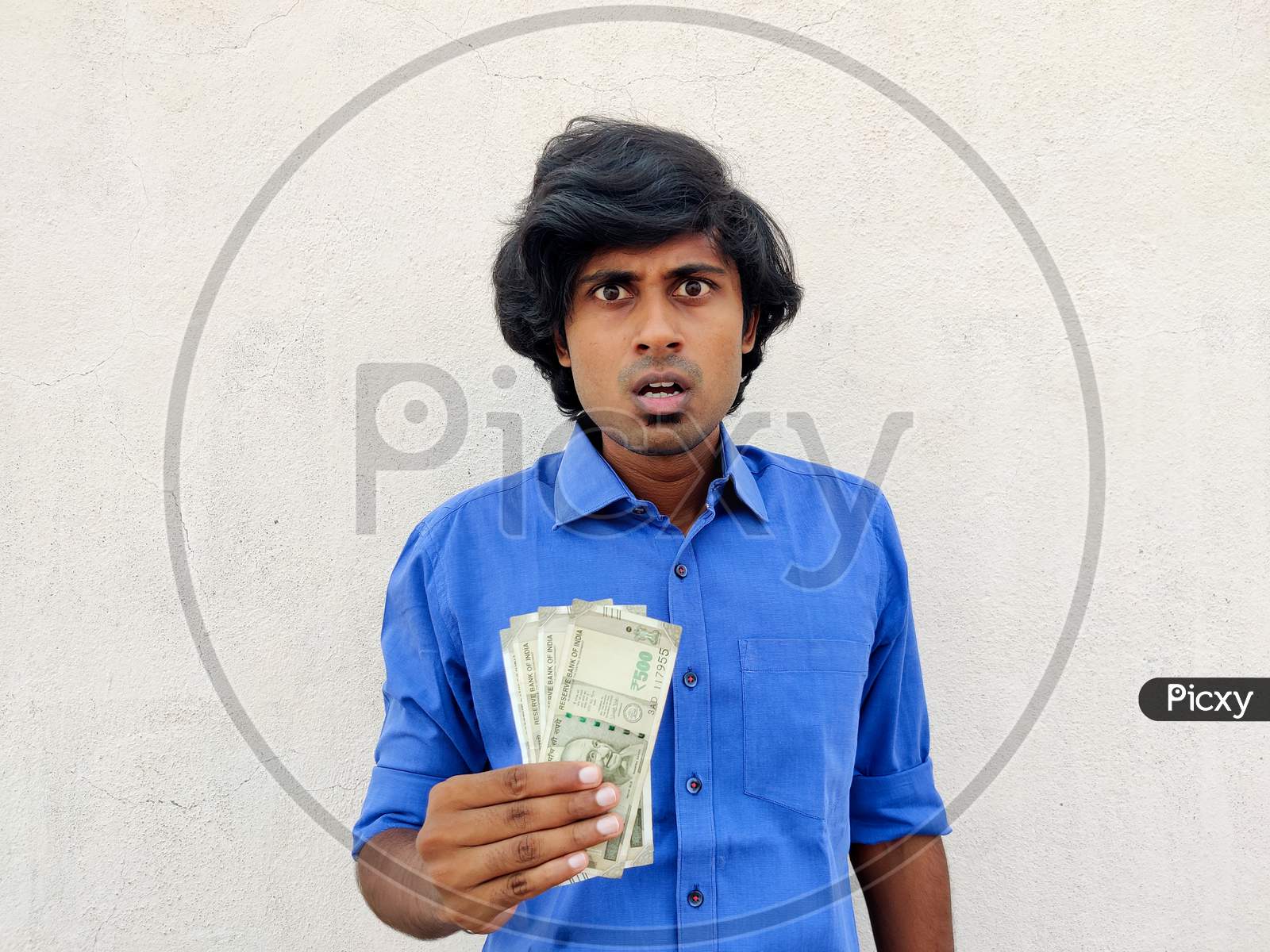 Shocking Young Handsome Indian Man In Blue Shirt Holding Four 500 Rupees Notes. White Background