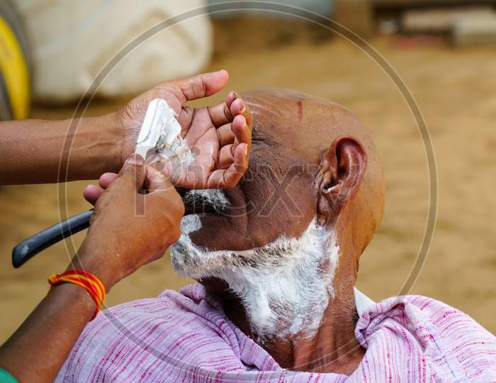 A Man Getting The Traditional Hair Cut At Home. Indian Barber Working On The Village Streets In A Sunny Day