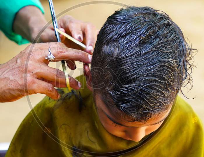 Indian Barber Working On The Village Streets In A Sunny Day. A Barber Cutting Hair Of Indian Boy During Lockdown In India.