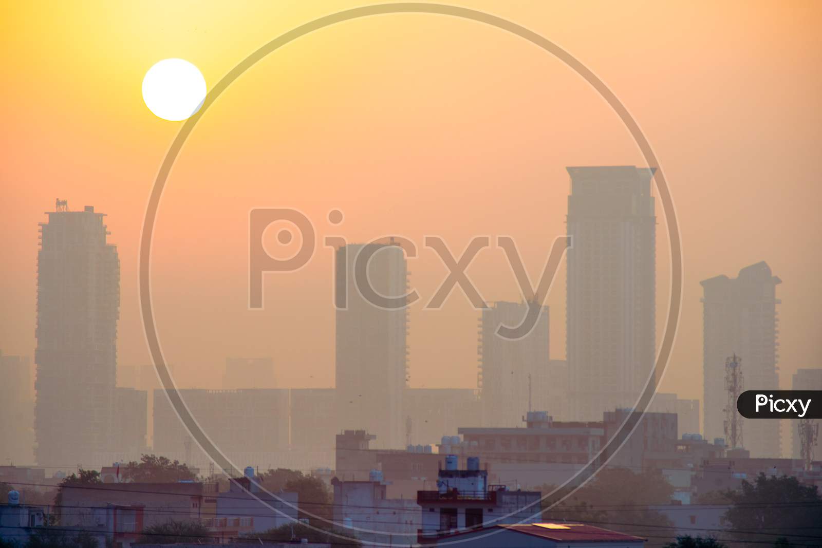Sun Rising Over Hazy Foggy Skyscrapers With Multi Floor Tall Buildings With Smaller Houses In The Foreground In The City Of Bangalore Hyderabad Gurgaon And Other Indian Cities