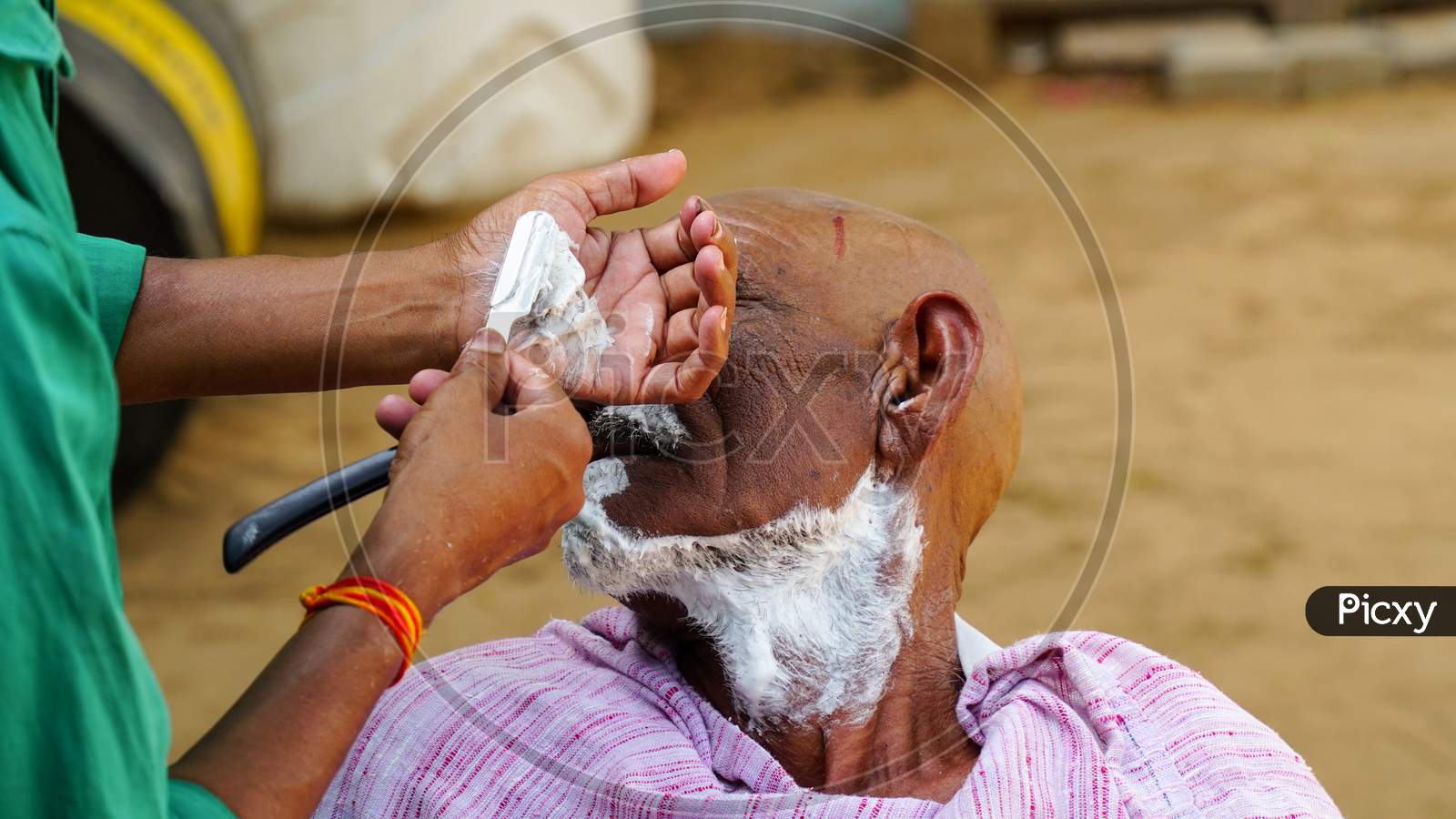 A Man Getting The Traditional Hair Cut At Home. Indian Barber Working On The Village Streets In A Sunny Day