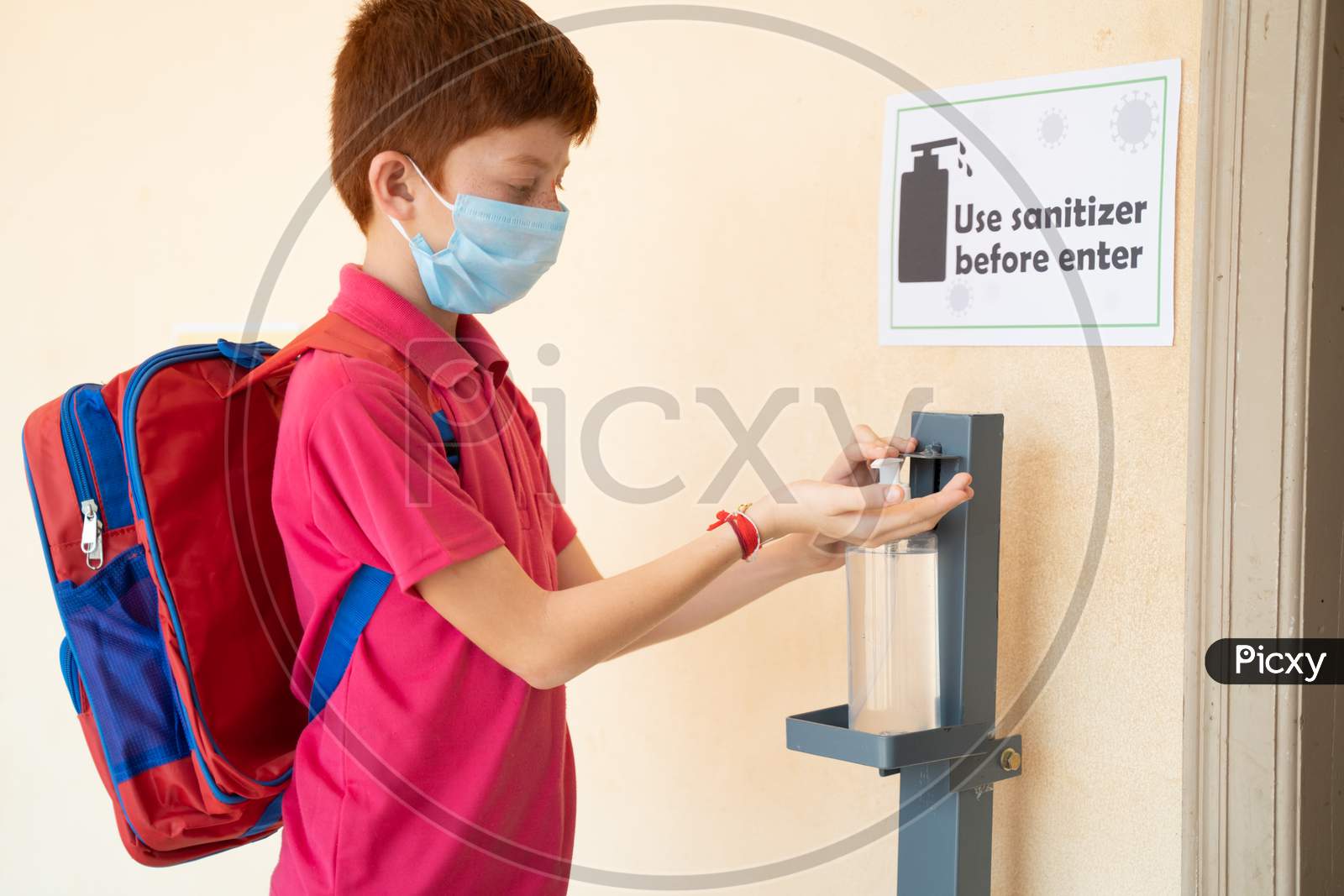 Focus On Sanitizer, Kid With Medical Mask Using Hand Sanitizer Before Entering Classroom - Concept Of Back To School Or School Reopen With Coronavirus Or Covid-19 Safety Measures.