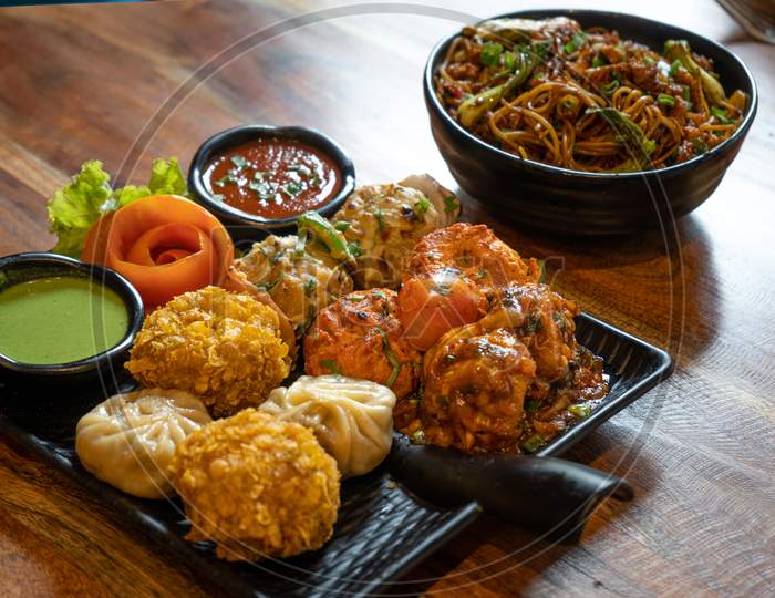 Fusion Of Indian Nepali Tibetan Chinese Cooking Of Fried Tandoori Roasted Grilled Momos With Sauces Noodles On A Black Plate And Wooden Table