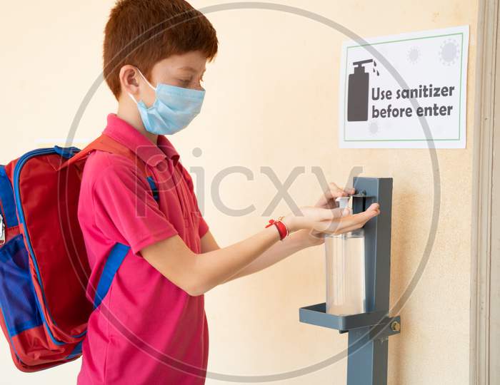 Focus On Sanitizer, Kid With Medical Mask Using Hand Sanitizer Before Entering Classroom - Concept Of Back To School Or School Reopen With Coronavirus Or Covid-19 Safety Measures.