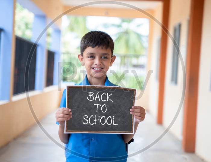 Smiling Young Kid Looking Camera And Showing By Back To School Sign Board School At Corridor - Concept Of School Reopen And Back To School.
